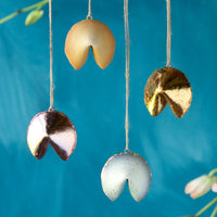 Four metallic fortune cookies hanging against a blue background